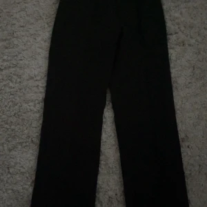 Svarta kostymbyxor från Madlady - Svarta kostymbyxor från Madlady i storlek EU32-Short. Byxorna har en klassisk rak passform med hög midja och vida ben. Perfekta för en clean och stilren look. Materialet känns mjukt och följsamt, vilket gör dem bekväma att bära hela dagen.