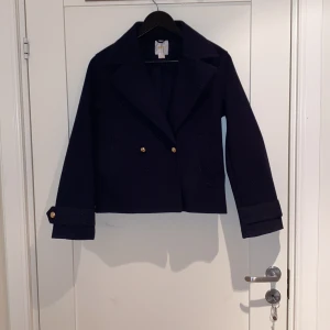 Mörkblå skepparkavaj från Gina Tricot - Snygg mörkblå jacka  från Gina Tricot med guldknappar framtill och på ärmsluten. Jackan har klassisk krage, raka linjer och är croppad i modellen. Säljer jackan för att den är för liten, har använt några gånger.