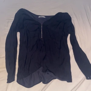 Svart långärmad blus från Gina Tricot - Snygg svart blus från Gina Tricot med v-ringning och dragkedja framtill. Långärmad modell i lätt och tunt material som faller snyggt. Perfekt för dig som gillar stilrena och enkla plagg med en twist.