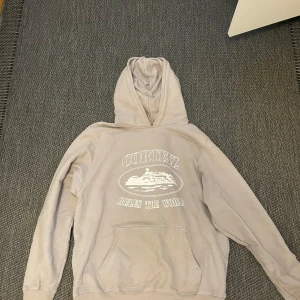 Beige hoodie Corteiz - Säljer en beige hoodie från Cortez med vit text och tryck på bröstet. Tröjan har huva, magficka och långa ärmar. Perfekt för dig som gillar streetwear och vill ha en chill look.