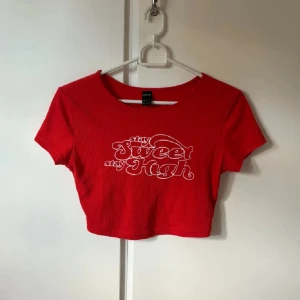 Röd croppad topp från SHEIN - Säljer en röd croppad topp från SHEIN med vit text 'stay sweet stay high' framtill. Toppen är ribbad, har rund halsringning och korta ärmar. Perfekt för dig som gillar en färgstark och trendig stil.