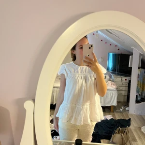 Vit blus med volang och spetsdetaljer - Säljer en söt vit blus med volang nertill och vid ärmslut. Blusen har fina spetsdetaljer och är tillverkad i ett tunt, luftigt tyg. Perfekt för dig som gillar romantisk och bohemisk stil. Rund halsringning och korta ärmar med lätt rynk.