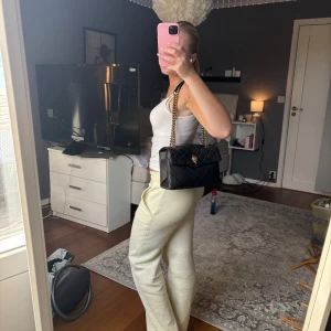 Svart quiltad axelväska Kurt Geiger - Snygg svart axelväska från Kurt Geiger i quiltat skinn med guldfärgade kedjor och ikonisk handdetalj på locket. Väskan har två stora fack och stängs med magnetlås. Perfekt storlek för det viktigaste och ger en lyxig vibe till din outfit.