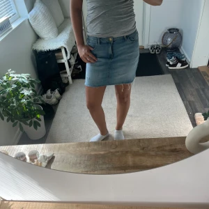 Ljusblå jeanskjol med rå kant - Säljer en ljusblå jeanskjol med klassisk femficksdesign och rå, fransad kant nedtill. Kjolen har knapp och dragkedja framtill och är i en kort modell som passar perfekt till sneakers eller sandaler. Enkel och snygg för dig som gillar denim. I barnstolen man passar ungefär storlek xs