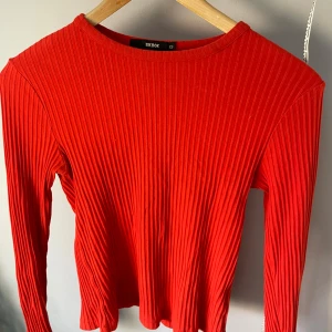 Röd ribbad långärmad tröja BikBok - Säljer en snygg röd långärmad tröja från BikBok i storlek XS. Tröjan är ribbad och har en tight passform med rund halsringning. Perfekt att styla med jeans eller kjol för en trendig look.