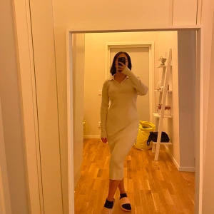 Beige stickad långklänning med krage - Säljer en beige stickad långklänning med lång ärm och snygg krage. Klänningen har en ribbad struktur och sitter figurnära utan att vara för tight. Perfekt för dig som gillar en enkel men stilren look.