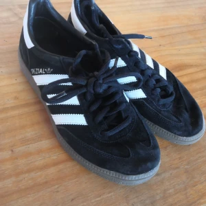 Adidas Spezial svarta sneakers mocka - Säljer ett par Adidas Spezial sneakers i svart mocka med klassiska vita ränder och vit häl. Skorna har snörning och en brun gummisula med snyggt mönster undertill. Perfekta för dig som gillar retrostil och streetwear. Storlek 36
