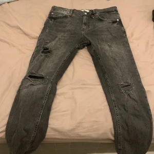 Svarta skinny jeans från Pull&Bear - Svarta skinny jeans från Pull&Bear med slitna detaljer och hål på benen. Jeansen har klassisk femficksdesign, knappgylf och är tillverkade i stretchig bomullsdenim. Perfekta för dig som gillar en edgy och trendig look. TAR BARA KONTANT SÅ SKRIV OM MÖTESPLATS 