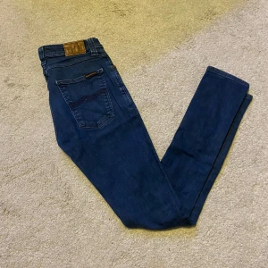 Nudie jeans - Säljer just nu ett par feta nudie jeans i toppskick! Dom är använda ett väldigt få tal gånger och är i väldigt bra skick. De är mörkblå med en mörk logga på bakfickorna. De är i storlek 28/32 och sitter perfekt.  Kontakta mig vid intresse!