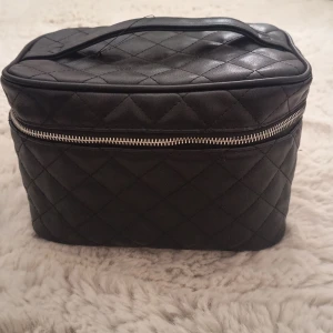 Svart quiltad handväska med dragkedja - Snygg svart quiltad handväska i syntetmaterial med silverfärgad dragkedja runt om och praktiskt handtag upptill. Väskan har en boxig form och är perfekt för att organisera dina grejer. Enkel men trendig design som passar till många stilar. Stor så man kan ha med sina saker på resor/ utflykter🩷