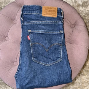 Levi's 724 High Rise Straight jeans blå - Snygga Levi's 724 High Rise Straight jeans i klassisk blå denim. Hög midja och raka ben ger en clean och tidlös look. Jeansen har fem fickor, gylf med dragkedja och är tillverkade i mjuk bomullsdenim. Perfekta för dig som gillar en enkel och stilren vibe. Uppsydda av butik för längd 150