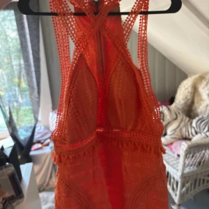 Orange spetsklänning Love Triangle - Superfin orange kortklänning från Love Triangle med djup v-ringning, spetsdetaljer och smala axelband som korsas i ryggen. Klänningen har dragkedja bak och fransar vid midjan för extra detalj. Perfekt för sommarens alla tillfällen!