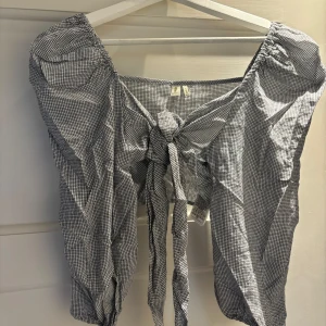 Rutig knytblus från ONLY - Säljer en blåvit rutig blus från ONLY i bomull. Toppen har trekvartsärmar, knytning framtill och en croppad passform. Perfekt för dig som gillar trendiga detaljer och en luftig känsla. Snygg till både jeans och kjol!