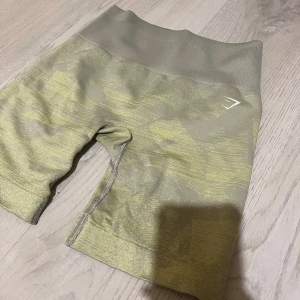 Gröna seamless shorts från Gymshark - Säljer ett par gröna seamless shorts från Gymshark med hög midja och ett subtilt mönster i ljusgrönt och beige. Stretchigt material som sitter tight och är perfekt för träning. Diskret logga på vänster höft. Supersnygga och bekväma för gymmet!