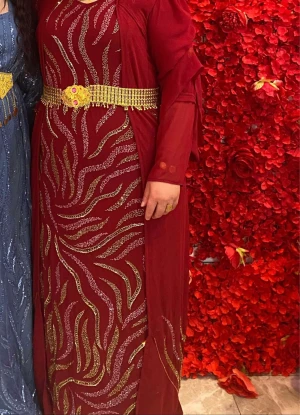 Kurdisk klänning i storlek L/XL - Säljer en vinröd långklänning i traditionell stil med glittriga guldmönster. Klänningen har lång ärm i transparent tyg och ett elegant fall. Perfekt för dig som vill sticka ut på festen!