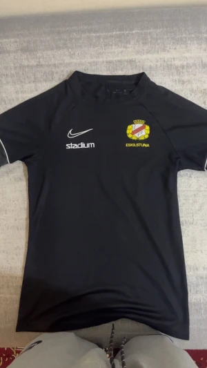 Svart Eskilstuna Södra FF Nike fotbollströja - Svart fotbollströja från Nike med Eskilstuna Södra FF klubbmärke på bröstet och vit Stadium-logga. Kortärmad modell med vita detaljer på ärmarna. Tillverkad i lätt och funktionellt material som andas bra under träning och match.