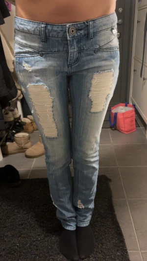 Ljusblå slitna jeans med raka ben - Säljer ett par ljusblå jeans från Only med snygga slitningar framtill och baktill. Jeansen har raka ben, klassisk femficksdesign och låg midja. Perfekta för dig som gillar en avslappnad och trendig look.