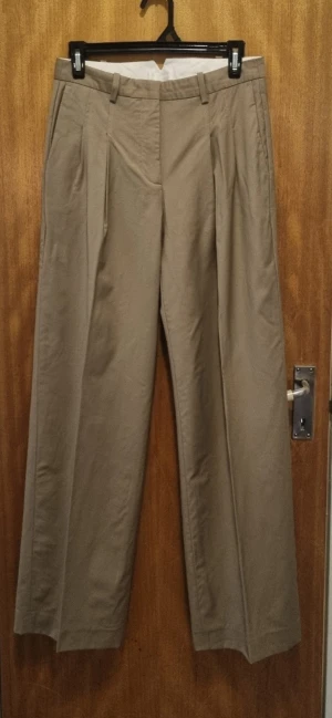 Beige kostymbyxor med pressveck - Snygga beige kostymbyxor med klassiska pressveck och bälteshällor. Byxorna har rak passform och är tillverkade i ett mjukt bomullsmaterial som ger en stilren look. Perfekta för dig som gillar en clean och enkel stil.