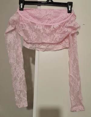 Ljusrosa spetsig offshoulder topp - Säljer en ljusrosa croppad topp med offshoulder-design och långa ärmar. Toppen är helt i spets med blommigt mönster och har en feminin, romantisk vibe. Perfekt för dig som gillar att sticka ut med detaljer och mjuka färger.
