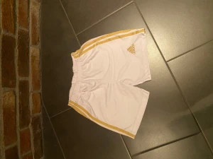 Guld/vit Adidas shorts - Hej, säljer mina adidas shorts som är för små. Storleken är 140. Skriv gärna om ni har frågor!