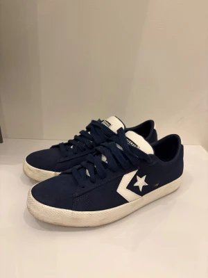 Mörkblå Converse CONS sneakers - Snygga mörkblå Converse CONS sneakers med vit stjärndetalj och logga på sidan. Skorna har rund tå, platt sula i gummi och klassisk snörning. Ovandelen är i mocka och tungan är vit med svart Converse-märke. Perfekt för dig som gillar retrostil och streetwear.