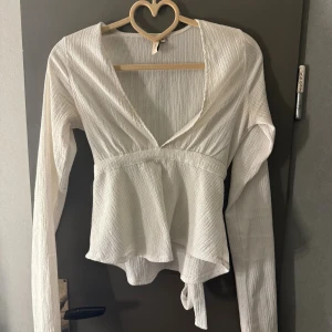 Vit omlottopp med knyt och v-ringning från Nelly - Säljer en vit omlottopp med lång ärm och v-ringad hals.  Sparsamt använd, inga skador!