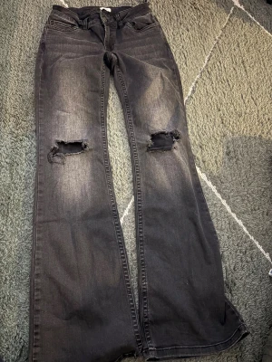 Svarta bootcut jeans från Nelly - Snygga svarta jeans med bootcut-modell och slitna hål på båda knäna. Jeansen är storlek 36!