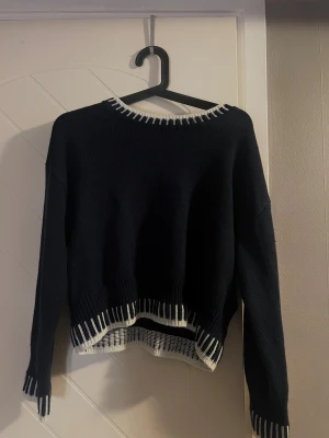 Mörkblåtröja med vit kant - Mörkblå tröja med vita detaljer vid halsringning, nederkant och ärmslut. Tröjan har en avslappnad passform och långa ärmar. 