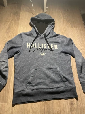 Vintage Hollister hoodie XS     Går ej ner i pris - VINTAGE,VÄLDIGT HÖG EFTERFRÅGAN EFTER SOM DET ÄR EN ÄLDRE MODELL MED FÅ EXEMPLAR. Snygg blå hoodie från Hollister i storlek XS med stor logga och texten 'California' på bröstet. Tröjan har huva med svarta snören, magficka och mjukt material på insidan. Perfekt för chill dagar och streetstyle.