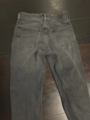 Mörkgrå Lee jeans straight fit - Snygga mörkgrå jeans från Lee med klassisk femficksdesign och raka ben. Jeansen har en diskret Lee-logga på bakfickan och är tillverkade i slitstarkt denimtyg. Passar dig som gillar en enkel och tidlös look.