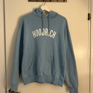 Ljusblå hoodie från Hoodrich XS - ‼️LÄS MIN BIO ‼️Snygg ljusblå hoodie från Hoodrich i storlek XS. Tröjan har vit HOODRICH-logga på bröstet, huva med snörning och en stor känguruficka framtill. Perfekt för en chill och avslappnad stil. Är oversized XS, så kan passa S,M också. Köpt från JD. 