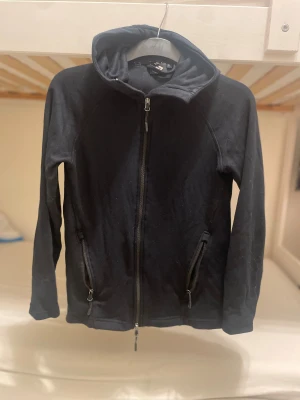 Svart hoodiejacka XS från lager 157 - Svart hoodie från lager 157 i storlek XS. Hoodien har hel dragkedja framtill, två sidofickor med dragkedja och en mjuk huva. Materialet är bomull och polyester, vilket gör den skön och lätt att bära. Perfekt för chill dagar och streetwear.