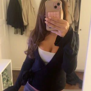 Svart omlottopp från Gina Tricot XS - Svart omlottopp från Gina Tricot i storlek XS. Toppen har långa ärmar, v-ringad hals och knyt i sidan för en snygg passform. Materialet är mjukt och stretchigt, perfekt för att skapa en clean och stilren look. Nypris: 299