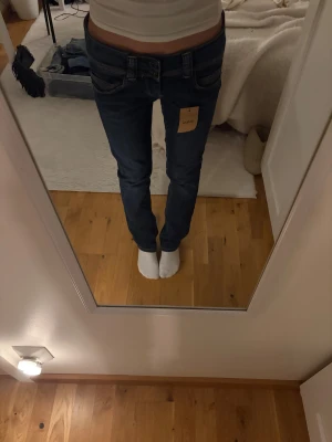 Pepe Jeans blå straight leg jeans - Snygga blå jeans från Pepe Jeans med låg midja och straight leg-passform. Klassisk femficksmodell med dubbla knappar i midjan och kontrastsömmar. Bakfickorna har broderad våg och logga. Perfekta för en avslappnad och cool stil.