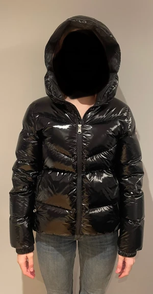 Svart glansig dunjacka från Colmar - Säljer en svart, glansig dunjacka från Colmar med stor huva och dragkedja framtill. Jackan har en puffig look, raka kanaler och Colmar-logga på ärmen. Perfekt för kalla dagar och riktigt snygg till jeans eller cargo.