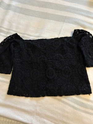 Svart spetsig offshoulder blus från Zara i XS  - Säljer en svart blus från Zara med offshoulder-design och trekvartsärm. Blusen är helspets med ett snyggt blommigt mönster och har en feminin, loose passform. Perfekt för dig som gillar detaljer och vill ha en cool, elegant look.