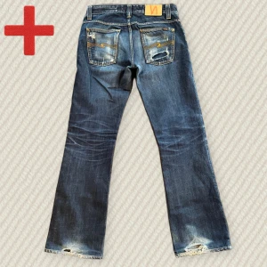 Vintage Nudie Jeans Bootcut Ola - Ett par riktigt feta Nudie Bootcut Ola i storlek 29/32! Riktigt fin bootcut passform som är riktigt trendigt just nu. Bra skick, men har slitningar som: heelbite, ett hål i högra bakfickan och några andra mindre. Skriv om du har frågor!  Mått: Midja – 41 cm, Lår – 27 cm, Innersöm – 77 cm, Yttersöm – 101 cm, Benöppning – 21 cm