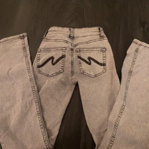 INTRESSEKOLL NELLY JEANS - Säljer ett par grå jeans från Nelly med coola svarta broderade detaljer på bakfickorna. Byxorna har klassisk femficksdesign och raka ben. Perfekt för dig som vill ha en unik look med snygga detaljer. De är i storlek 36 men passar även lite större och mindre storlekar för att de är stretchiga. De är lite slitna längst ner i benen men inget man tänker på. Skriv om det är något du undrar över eller om det behövs fler bilder. Priset kan även diskuteras 💞