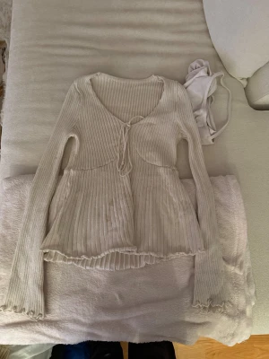 Ribbad ljusbeige långärmad topp - Säljer en superfin ljusbeige ribbad topp med lång ärm och v-ringning. Toppen har snörning framtill och volangkant vid ärmslut och nederkant. Materialet är mjukt och stretchigt, perfekt för en chill och snygg look.