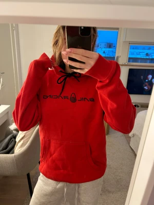 Röd Sail Racing hoodie med svart tryck - Röd hoodie från Sail Racing med svart logotyptryck på bröstet och svarta snören i huvan. Passar både tjej och kille, storlek M. Endast använd 1 gång så den är som ny💗
