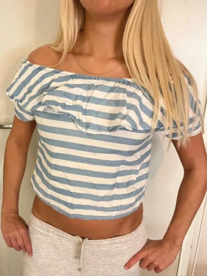Randig offshoulder croppad topp - Säljer en söt croppad topp med blå och vita ränder. Toppen har offshoulder-modell och en volangdetalj framtill. Toppen är från zaras barnavdelningen men det passar xxs-s💓