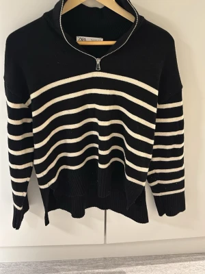 Svartvit randig stickad tröja Zara - Svart stickad tröja från Zara. Tröjan har en hög krage med half zip-dragkedja.