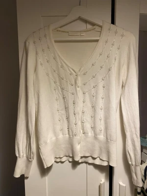 Vit kofta med broderi från Lindex - Supersöt vit kofta från Lindex i storlek S. Koftan har v-ringning, knappar framtill och fina broderade detaljer. Perfekt till båten och sommaren att ha över ett linne. Väldigt bra skick och inte synligt använd.🫶🏼