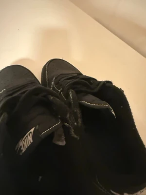 Black phantoms low  - Svarta Nike Air Jordan 1 sneakers med vita kontrastsömmar och broderade detaljer på hälen. Skorna har snörning, perforerad tå och rund sula. Materialet är skinn och syntet, och modellen är lows. Snygg broderad Air Jordan-logga och bi på baksidan.