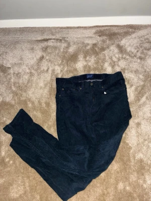 Svarta manchesterbyxor från GANT - Säljer ett par svarta manchesterbyxor från GANT med klassisk femficksdesign och snygga detaljer som läderpatch med logga bak. Byxorna har smal passform och dragkedja i gylfen. Perfekta för dig som gillar stilrena och bekväma byxor med lite edge. Köpte dem för 1599 kr på NK använt dem på dop och vigslar och den är i allra högsta grad ett bra alternativ till fester och annat. Hör av er vid köp. Den är small fast passar även mig som är M32/34
