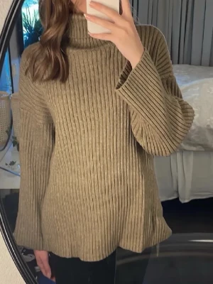 Beige ribbad polotröja stickad - Säljer en beige stickad polotröja med breda ribbade ränder. Tröjan har lång ärm, hög krage och slits på sidorna vilket ger en chill och loose passform. Perfekt för lager-på-lager under hösten och vintern.