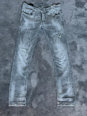 Grå dondup jeans med slitningar - Snygga grå jeans med skinny passform och slitna detaljer på benen och vid grenen. Jeansen har klassisk femficksdesign, knappgylf och en tvättad look. Dom har dock ett hål vid skrevet men det är inte så synligt 