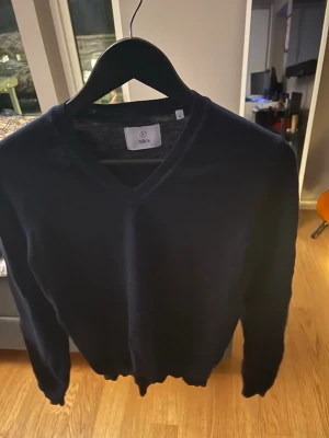 Mörkblå v-ringad tröja från Bläck - Snygg mörkblå v-ringad tröja från Bläck i mjukt material. Perfekt att slänga på sig när det är lite kyligt ute. Tröjan har långa ärmar och en klassisk passform som funkar till många olika stilar.