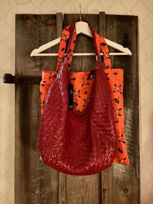 Röd axelväska i flätat skinn från Adax, färg Amaretto - Säljer en snygg röd axelväska från Adax, modell Salemo Mindy (i färgen Amaretto). Väskan är tillverkad i flätat skinn och har en mjuk, rundad form med breda handtag. Perfekt för dig som vill ha en stilren och trendig väska med plats för allt du behöver. Mått: 42x24x13 cm. Medföljer en korthållare i samma färg samt äkthetsintyg och dustbag. Knappt använd och prislappen finns kvar och medföljer.