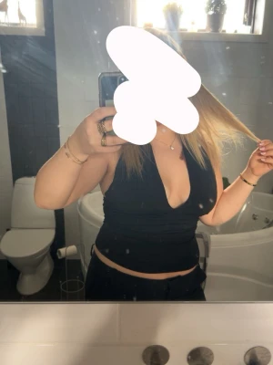 Svart omlott topp med djup v-ringning - Säljer en svart omlott topp med djup v-ringning och croppad passform. Toppen är ärmlös och har en stilren look som passar perfekt till jeans eller kjol. Materialet känns mjukt och följsamt mot kroppen. Perfekt för dig som gillar att sticka ut med en enkel men snygg topp.